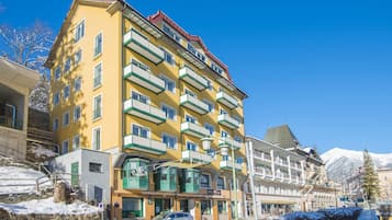 A multi-story hotel with balconies, a stone facade, and a mountain backdrop.