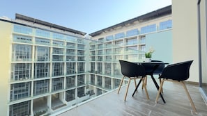 A modern building with large glass windows, a balcony with a table and chairs, and a view of the surrounding area.
