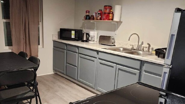 Une cuisine compacte équipée d’une cuisinière, d’un four à micro-ondes et d’un évier. On y trouve une table à manger avec des chaises, ainsi qu’une fenêtre avec des rideaux.