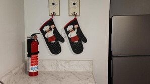 Une cuisine équipée d’un évier en acier inoxydable, d’un extincteur rouge et de deux maniques de four décorées sur le thème des chefs, accrochées au mur.