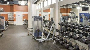 Une salle de sport équipée de divers appareils d’exercice, notamment des haltères et des machines de musculation, disposés dans un espace vaste et bien aménagé.