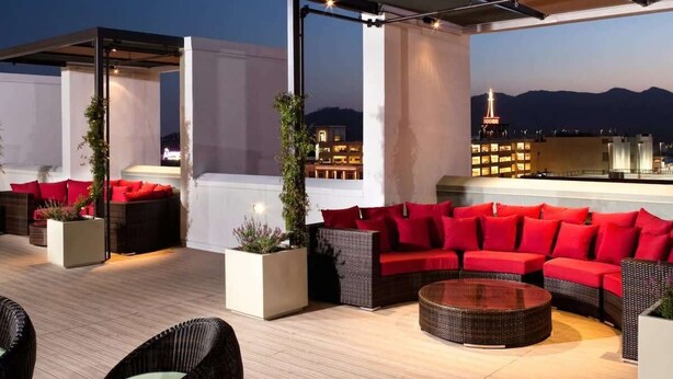 Un salon sur le toit avec des espaces de détente en plein air, comprenant des canapés et des fauteuils, ainsi qu’un bar.
