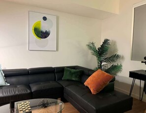 A modern living room with a black leather sectional sofa, a glass coffee table, and a large abstract painting.