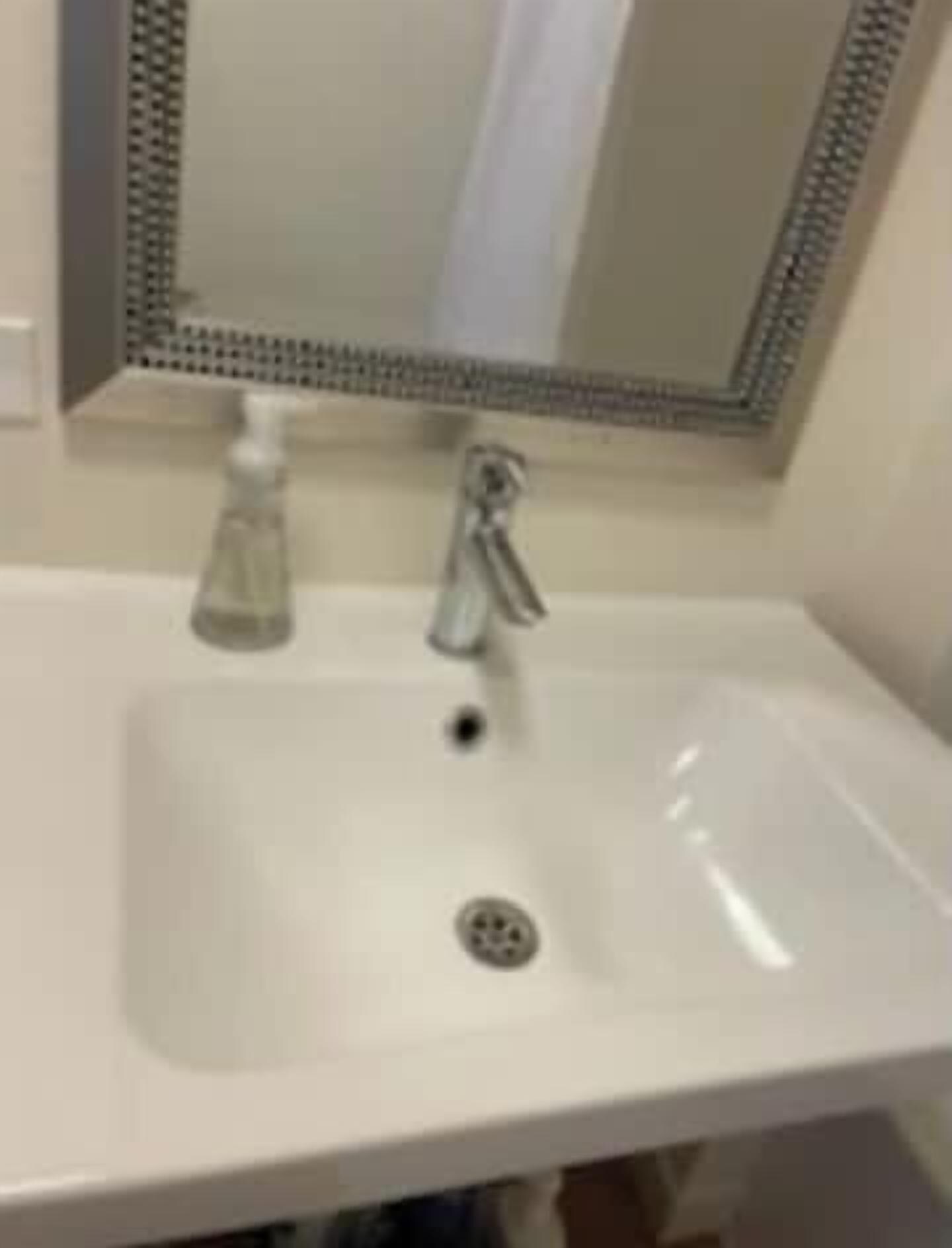 A white bathroom sink with a mirror above it, a faucet, and a soap dispenser.