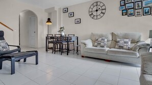 A modern living room with a sofa, a dining table with chairs, a bench, and a large wall clock. - Capitulaciones - Swimming pool, garage, 3 bedrooms, terrace (Torremolinos)