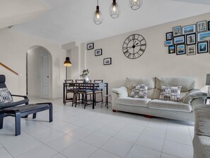 Ein modernes Wohnzimmer mit einer Couch, einem Esstisch mit Stühlen, einer Bank und einer großen Wanduhr.