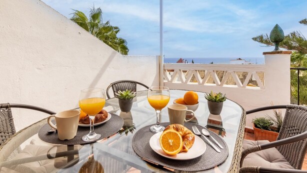 A glass table with breakfast items, including orange juice, croissants, and a plate with an orange slice, set on a balcony overlooking the sea. - Capitulaciones - Swimming pool, garage, 3 bedrooms, terrace (Torremolinos)