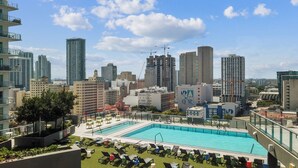 Piscina no terraço com espreguiçadeiras, rodeada por edifícios altos e um céu claro.