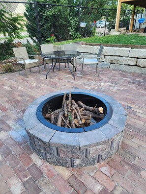 A circular stone fire pit with logs, surrounded by a brick patio. - Spacious Fully Renovated  Apt, near State Capitol Bldg, Downtown Topeka, I-70 (Topeka)