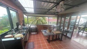 A kitchen with a stove, sink, and large windows overlooking a garden. - Golden Mango House (Sam Roi Yot)