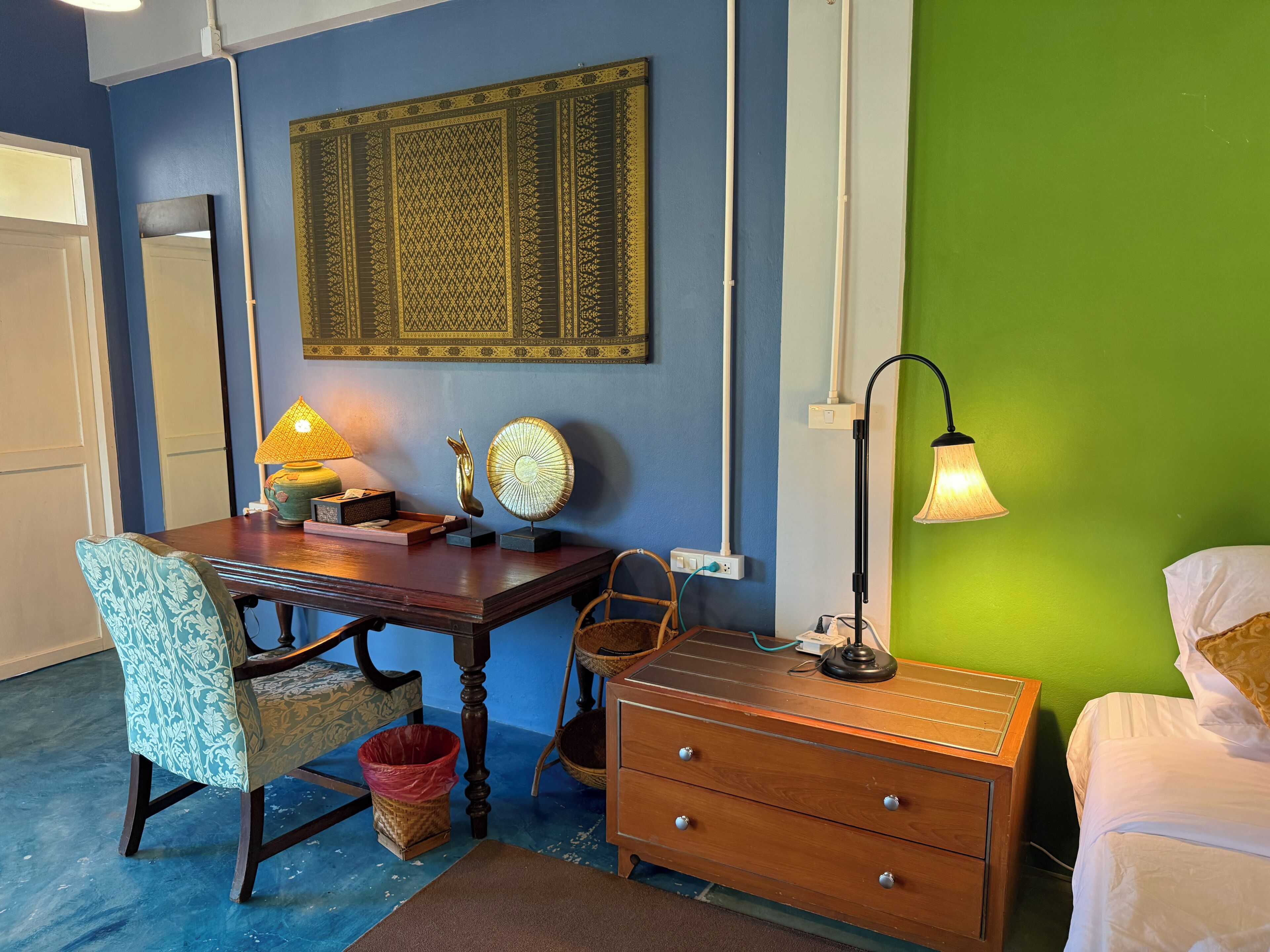 A room with a desk, chair, lamp, and a bed.