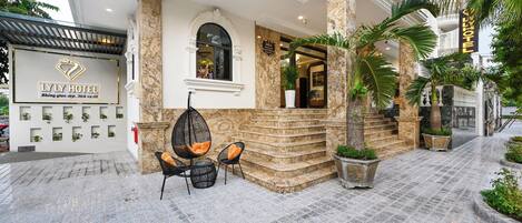 The exterior of LLY Hotel with a stone facade, a covered entrance, and outdoor seating.