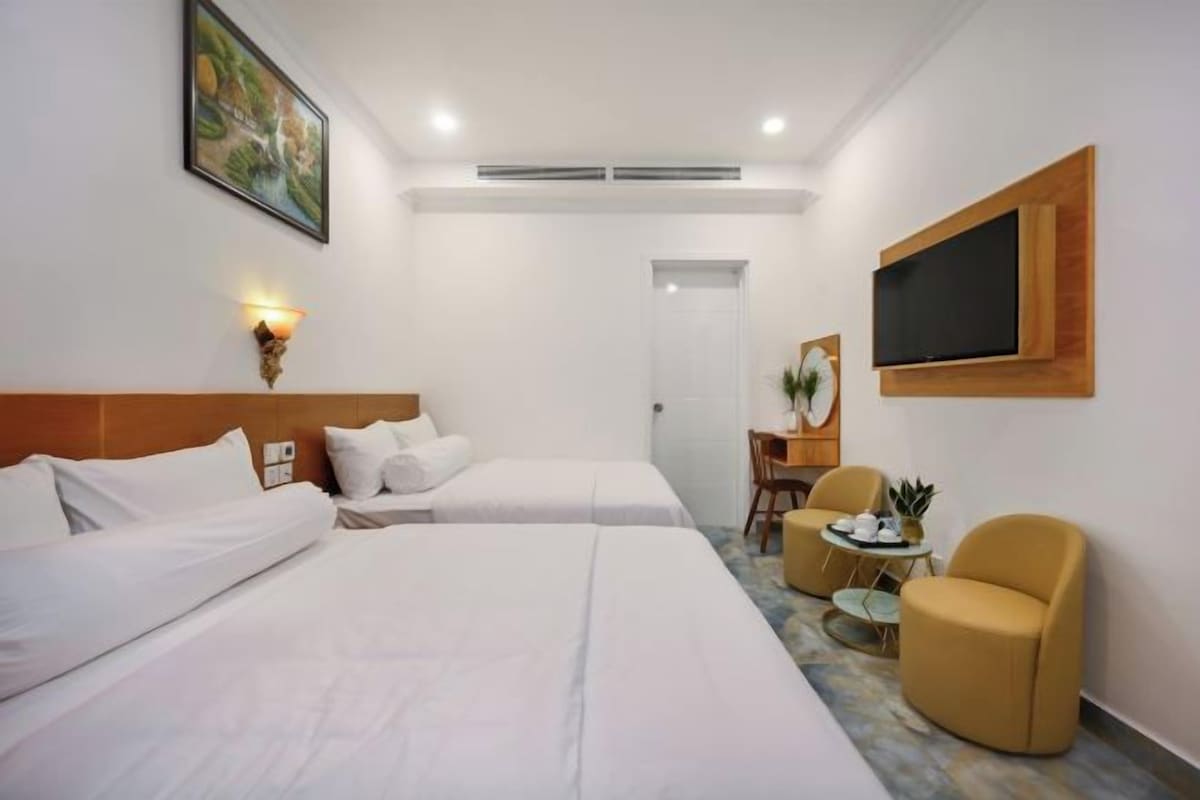 Una camera d'albergo con due letti, una scrivania, una sedia e una TV a parete.