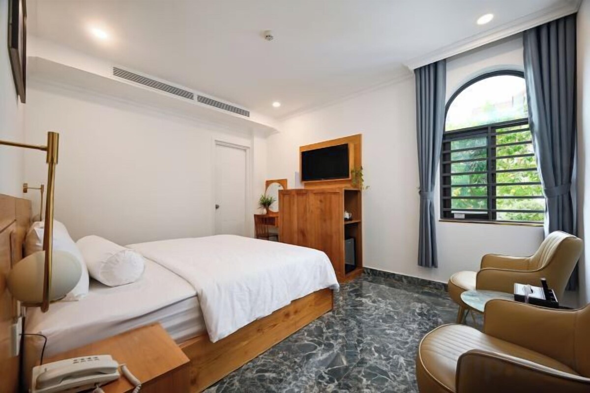 Een hotelkamer met een bed, bureau, stoel, televisie en raam met gordijnen.
