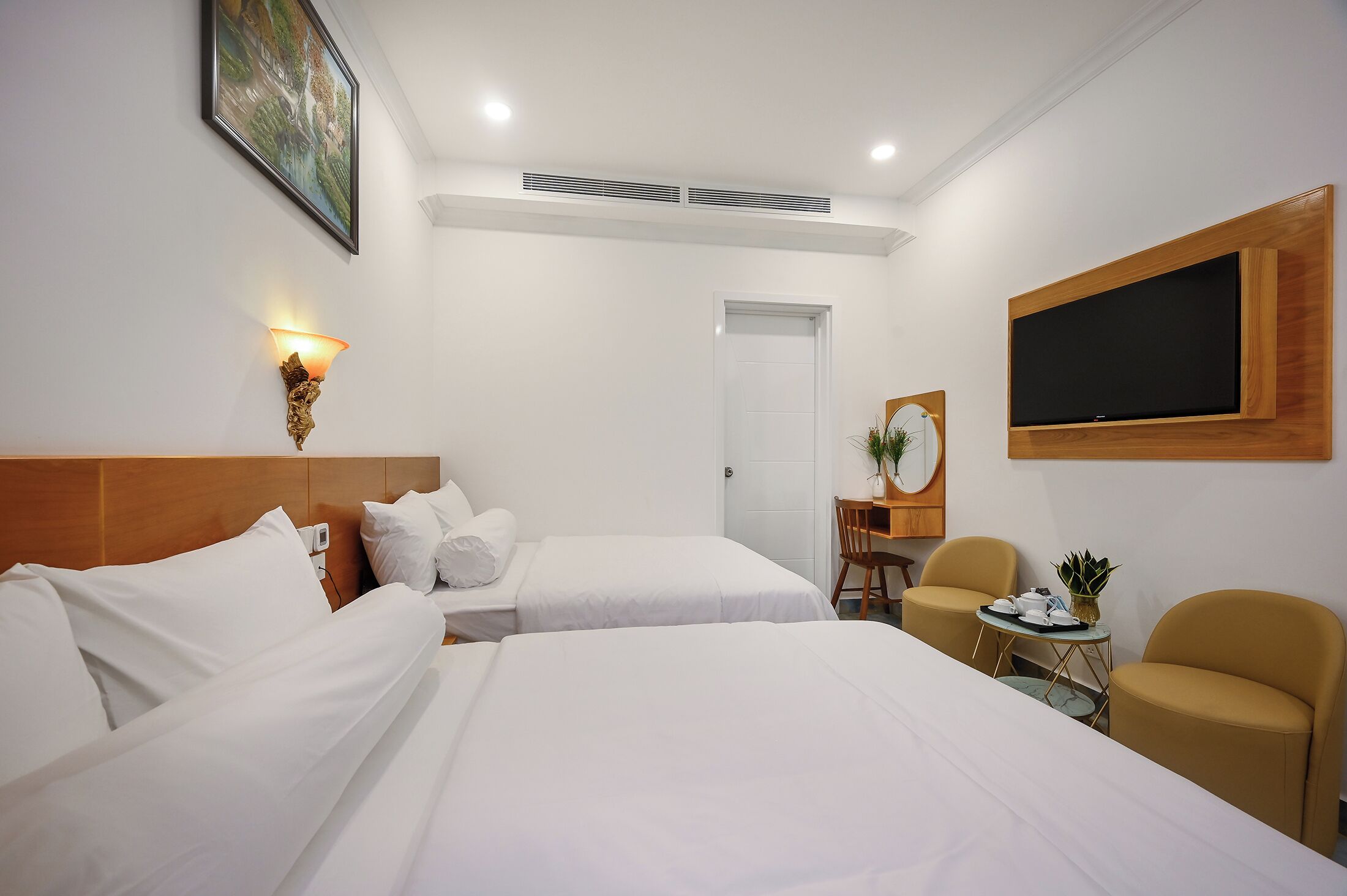 A hotel room with two beds, a desk, a chair, a TV, and a painting on the wall.