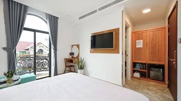 Habitación de hotel con cama, escritorio con silla, televisor montado en la pared, armario y balcón con vistas a edificios.