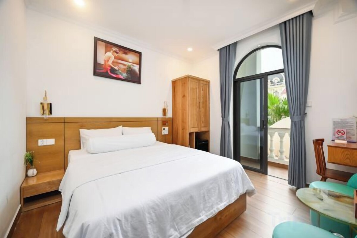 A hotel room with a bed, a wooden headboard, a nightstand, a desk, and a view of the outdoors.