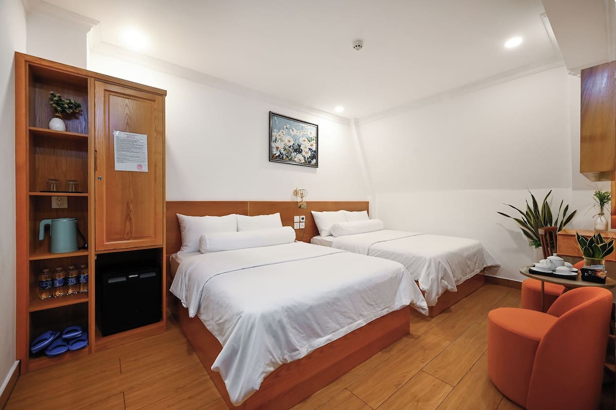 Camera d'albergo con due letti, un armadio in legno, un tavolino con una pianta e una sedia.