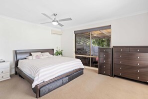 A bedroom with a bed, a dresser, a ceiling fan, and a window with a view of the outdoors. - Waterfront Canal Escape in Burleigh (Burleigh Waters)