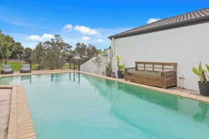 A swimming pool with a wooden bench and potted plants, surrounded by a white building and a fence. - Waterfront Canal Escape in Burleigh (Burleigh Waters)