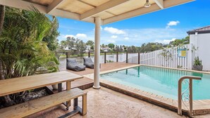 A pool area with a wooden deck, benches, and a poolside railing. - Waterfront Canal Escape in Burleigh (Burleigh Waters)