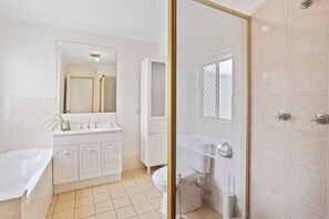 A modern bathroom with a white vanity, a large mirror, a bathtub, and a shower area. - Waterfront Canal Escape in Burleigh (Burleigh Waters)