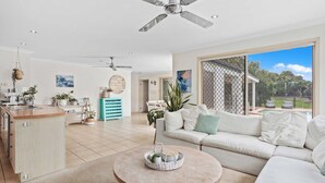 A spacious living area with a round coffee table, a sofa, and a kitchen area with a countertop and sink. - Waterfront Canal Escape in Burleigh (Burleigh Waters)