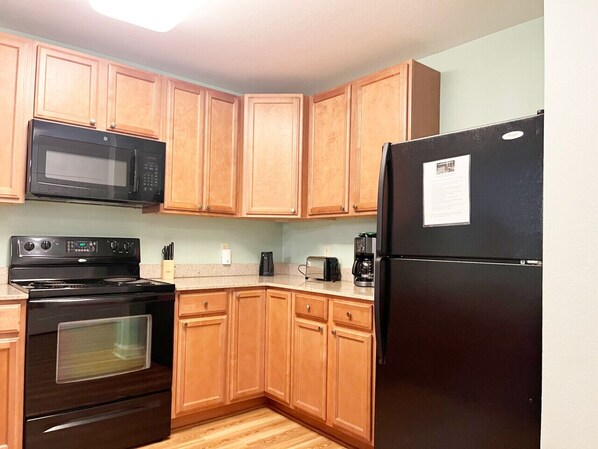 A kitchen with wooden cabinets, a black microwave, a stove, a refrigerator, and a countertop with a coffee maker and toaster.