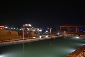 A nighttime swimming pool area with lounge chairs and a building in the background. - Grandeur's Tiger Estate (Yamkeshwar)