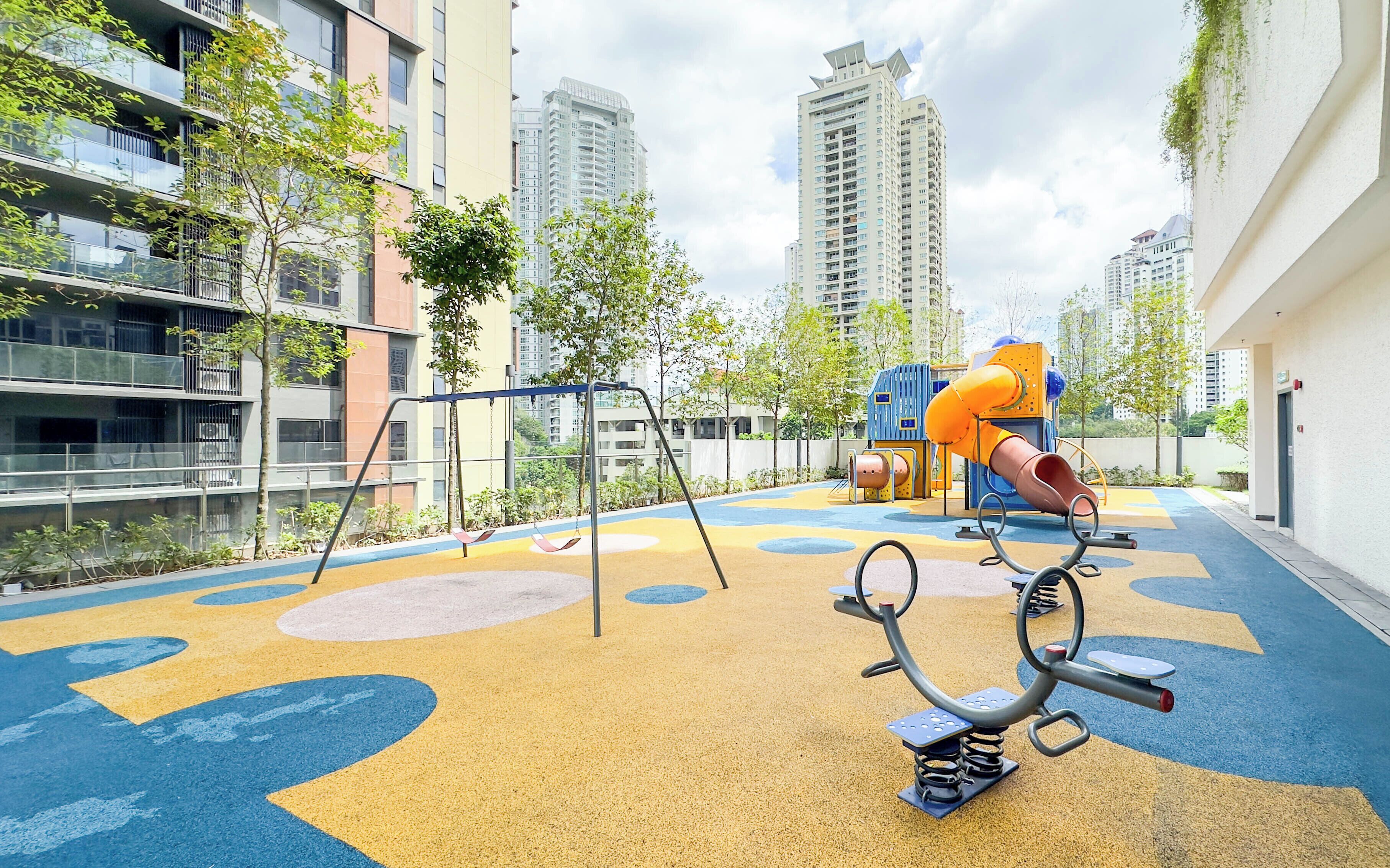 An outdoor playground with swings, slides, and climbing structures, surrounded by high-rise residential buildings.