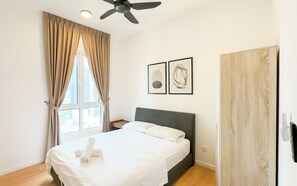 Un dormitorio con cama, ventilador de techo, ventana con cortinas y dos cuadros en la pared.