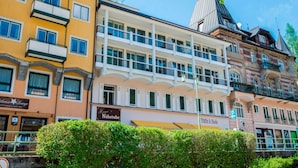 Un edificio de varios pisos con balcones, un restaurante llamado "Hermi's Nähstube" y un letrero que dice "Tracht & Mode".
