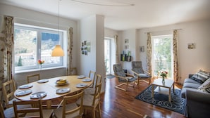 Un comedor con mesa y sillas de madera, un sofá y un balcón con cortinas.