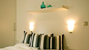 Una cama bien tendida con almohadas a rayas, una mesita de noche con velas y apliques de pared.