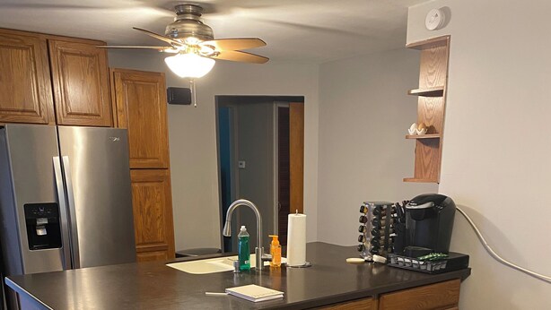 A kitchen with wooden cabinets, a stainless steel refrigerator, a sink, a coffee maker, and a vase with flowers on the island.