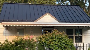 A house with a dark metal roof, a front porch, and a well-maintained lawn.
