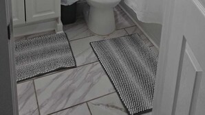 A bathroom with a toilet, sink, and shelves above the toilet. There is a shower curtain and a mirror on the wall.