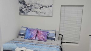 A bedroom with a bed, a ceiling fan, a window with blinds, and a wall-mounted artwork.