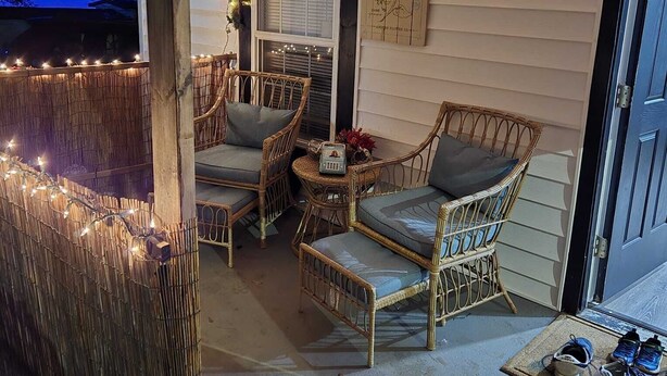 A porch with wicker chairs and a small table, decorated with string lights and garlands.