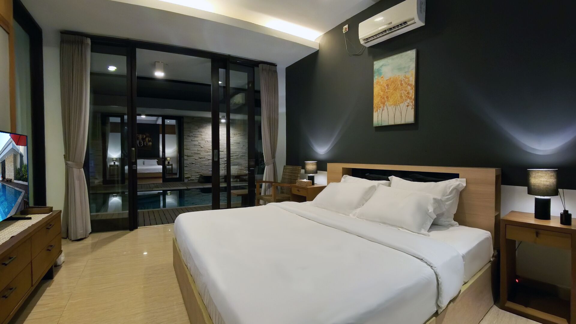 A modern hotel room with a large bed, a television, a desk, and a view of a pool through a glass door.