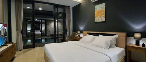 A modern hotel room with a large bed, a television, a desk, and a view of a pool through a glass door.