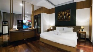 Habitación de hotel moderna con una cama grande, un escritorio con una computadora, un televisor y un cuadro de elefantes en la pared.