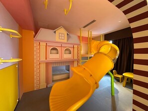 Zona de juegos infantiles con un tobogán, estructuras de juego y una casita.