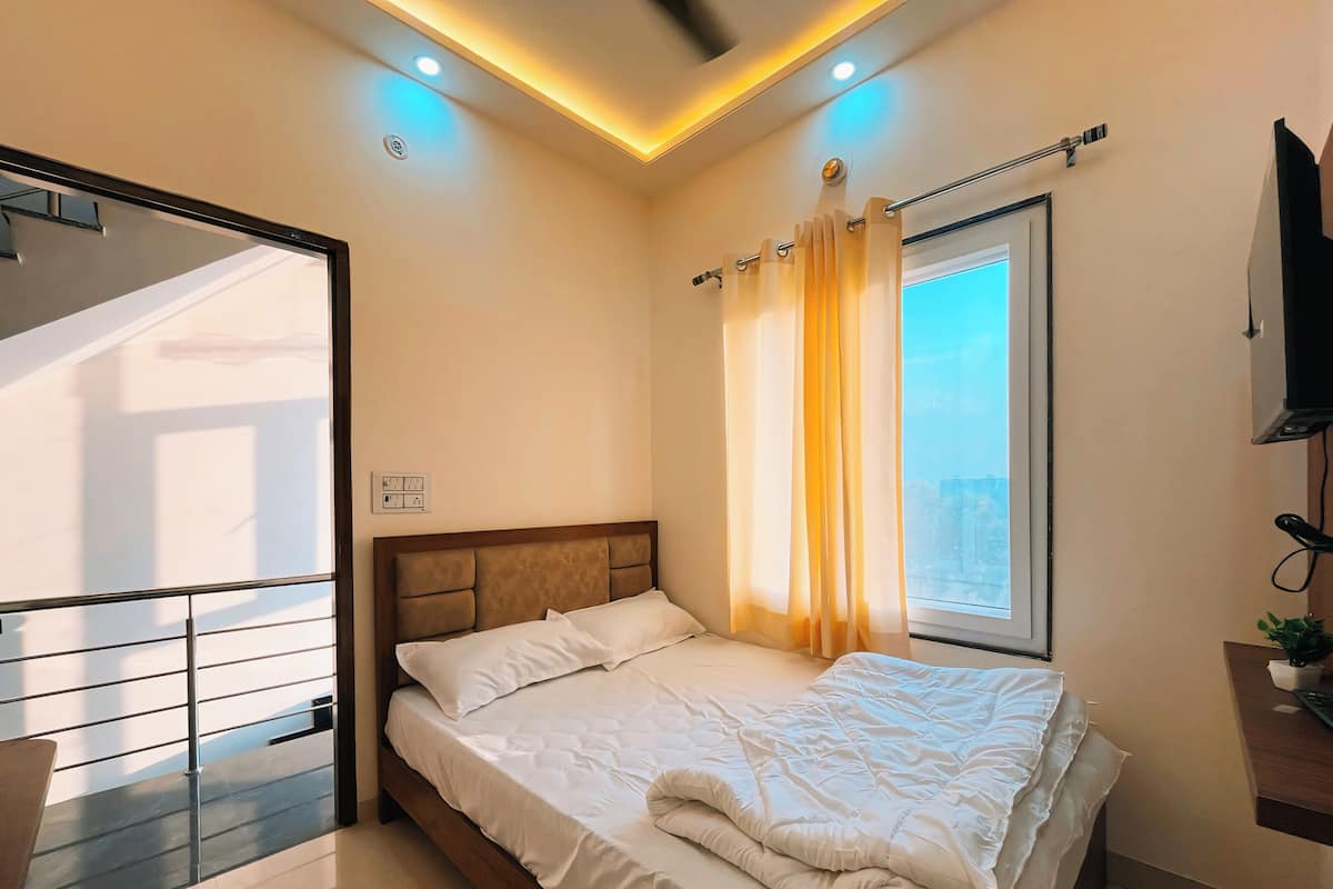 Une chambre à coucher avec un lit, une fenêtre avec des rideaux, un téléviseur et un luminaire au plafond.