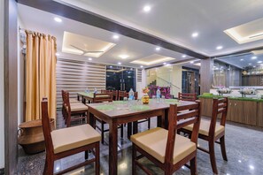 A dining area with a long table set for multiple people, wooden chairs with cushioned seats, and a modern ceiling design with recessed lighting. - Treebo Sri vi ka Residency (Puducherry)