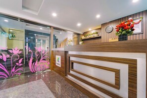A reception area with a wooden reception desk, a clock, and a vase of red flowers. - Treebo Sri vi ka Residency (Puducherry)