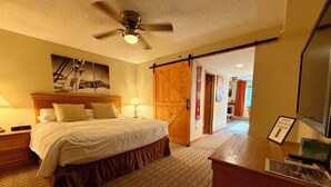 Habitación de hotel con cama, lámparas de noche, ventilador de techo, puerta de madera y escritorio con un letrero que indica que los pases de estacionamiento están en el cajón.