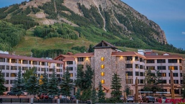 Un hotel con varias construcciones, una imponente torre de piedra y una montaña al fondo.