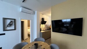 A modern living room with a round wooden dining table, grey upholstered chairs, a mounted flat-screen TV, and a framed trumpet on the wall. - Apartment Urban Living (Porec)