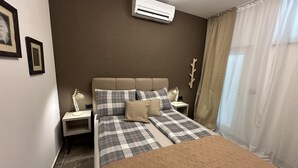 A bedroom with a bed, two bedside tables, a wall-mounted air conditioner, and a window with curtains. - Apartment Urban Living (Porec)